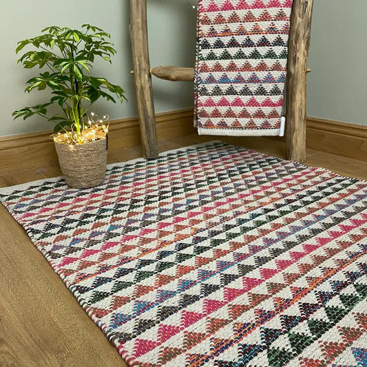 A cotton rug with an off white background and covered in a repeat pattern of bunting in reds blues, rusts and greens. 90 x 150cm