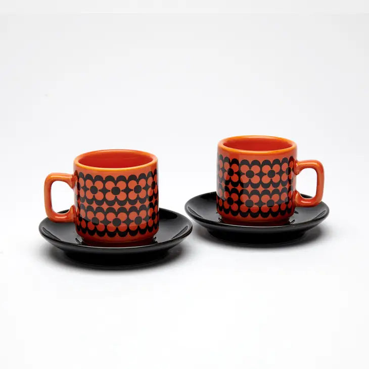 A dinky set of two espresso cups in a retro design. Orange background with black flower design and black saucers