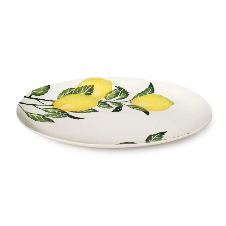  A large oval ceramic platter with a white background and featuring hand painted lemons ana green leaves. 